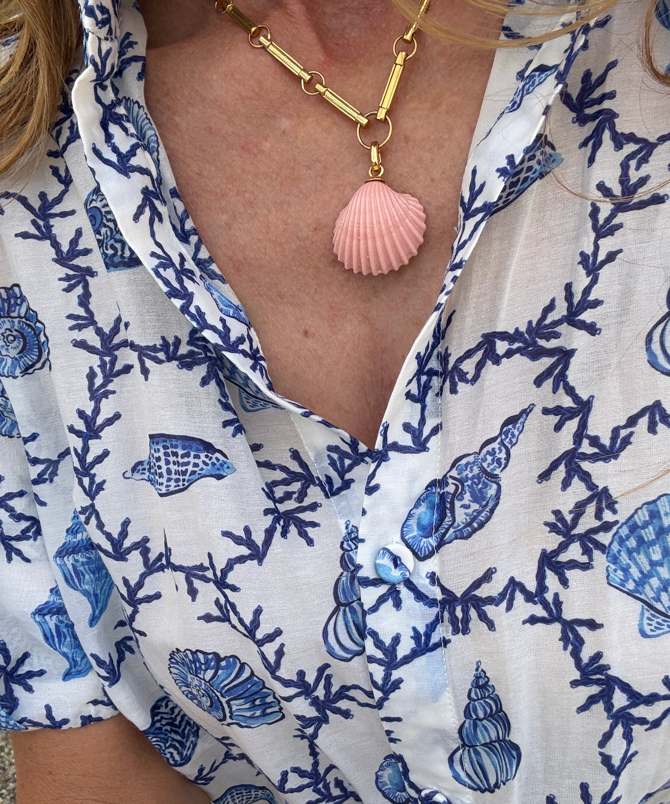 close up pink shell charm on gold chain being worn with blue shell print shirt 