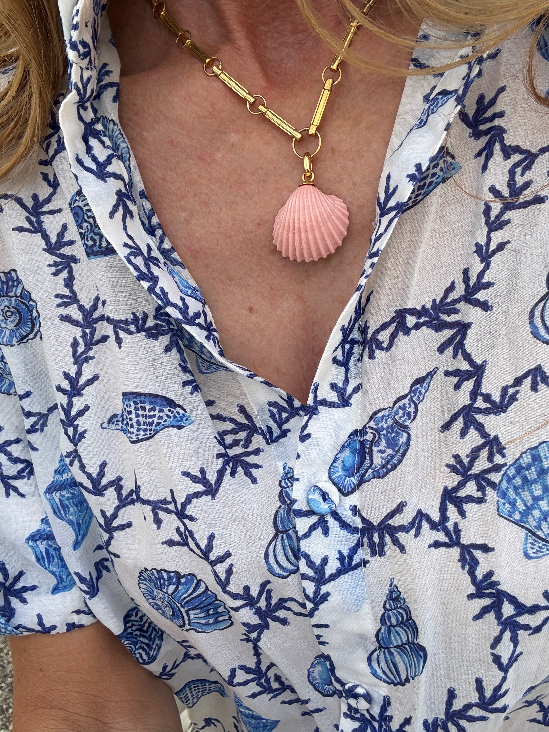 close up pink shell charm on gold chain being worn with blue shell print shirt 