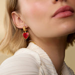 Close-up of a woman wearing gold earrings with red heart charms.