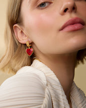 Close-up of a woman wearing gold earrings with red heart charms.