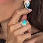 Close-up of a person wearing turquoise stone jewelry including earrings and a ring.