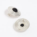 Pair of silver round earrings with black onyx stones in the centre, on a white background. Image shows reverse of earrings