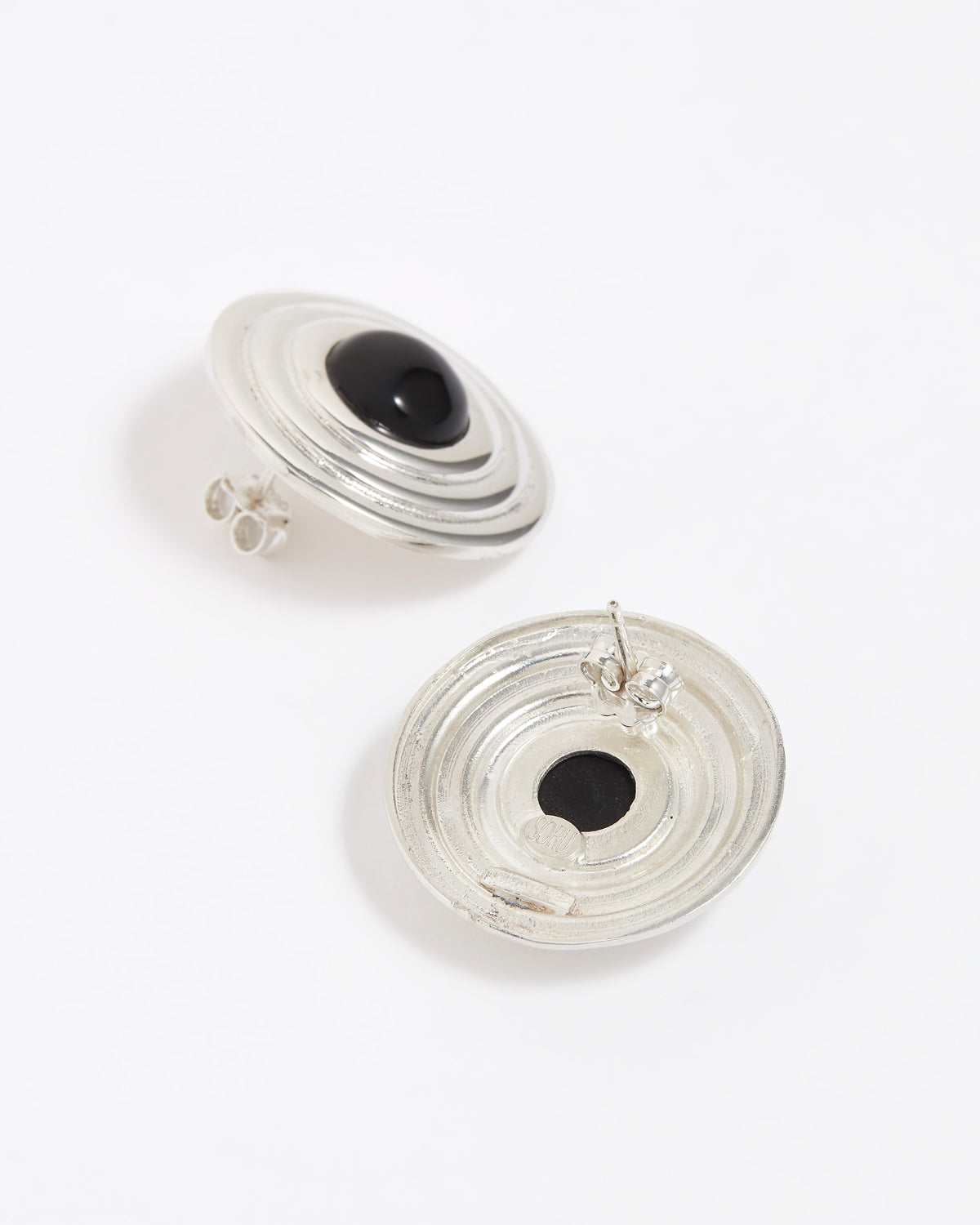 Pair of silver round earrings with black onyx stones in the centre, on a white background. Image shows reverse of earrings