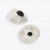 Pair of silver round earrings with black onyx stones in the centre, on a white background. Image shows reverse of earrings