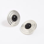 Pair of silver round earrings with black onyx stones in the centre, on a white background