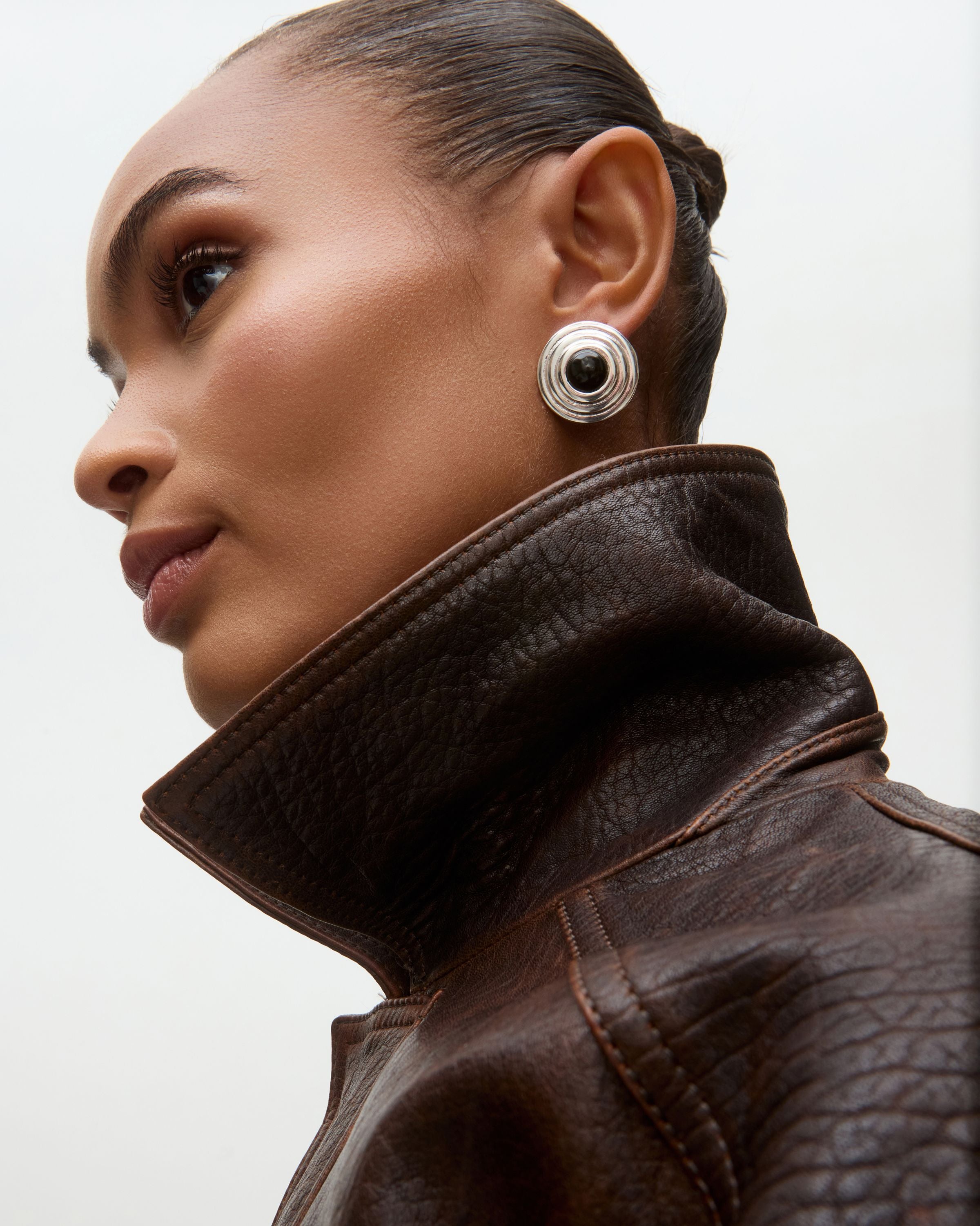 Woman wearing a brown leather jacket and silver earrings on a light gray background