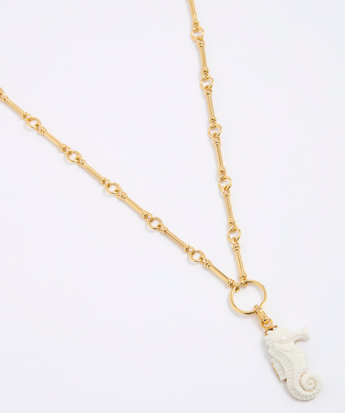 Gold necklace with a white seahorse pendant on a light gray background