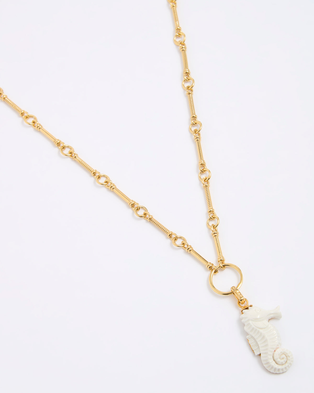 Gold necklace with a white seahorse pendant on a light gray background