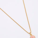 Gold coloured necklace with a pink pendant on a white background