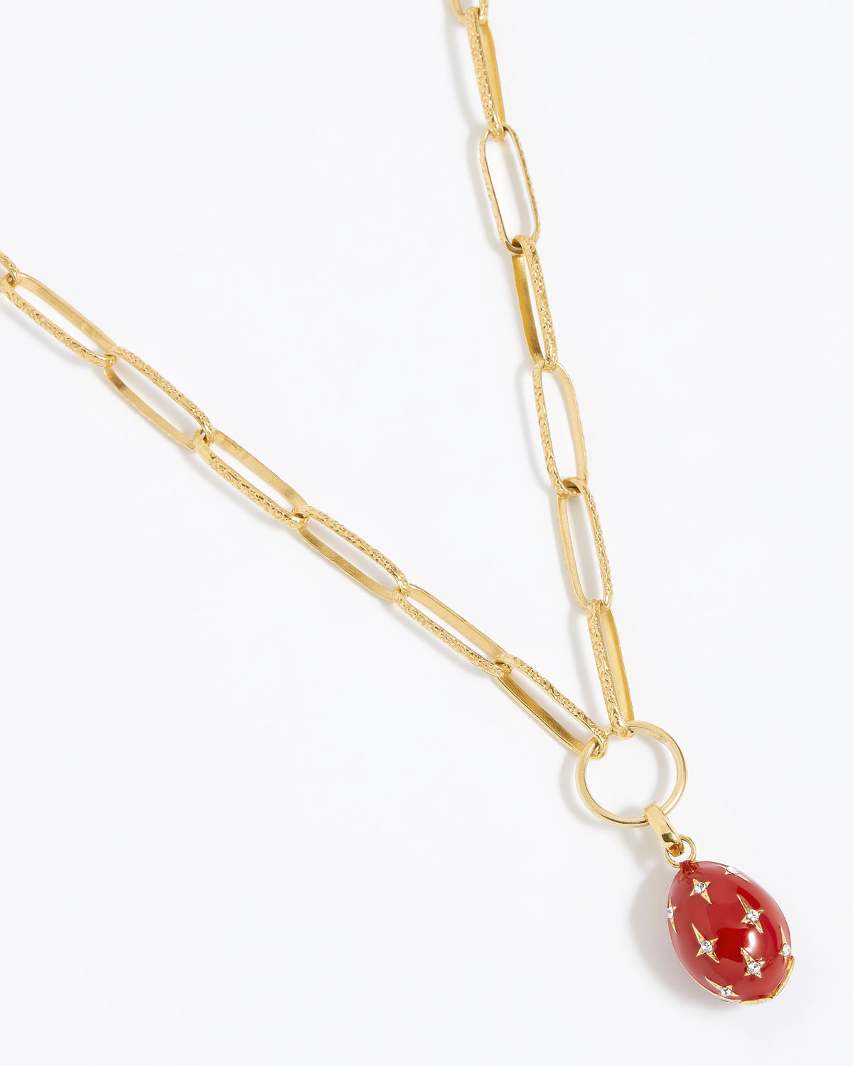 Red egg-shaped pendant with gold accents and crystal star designs attached to a gold charm chain,  on a white background