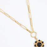 Gold circular charm pendant with central onyx stone with black and gold beaded edge hanging on a charm chain,  on a white background