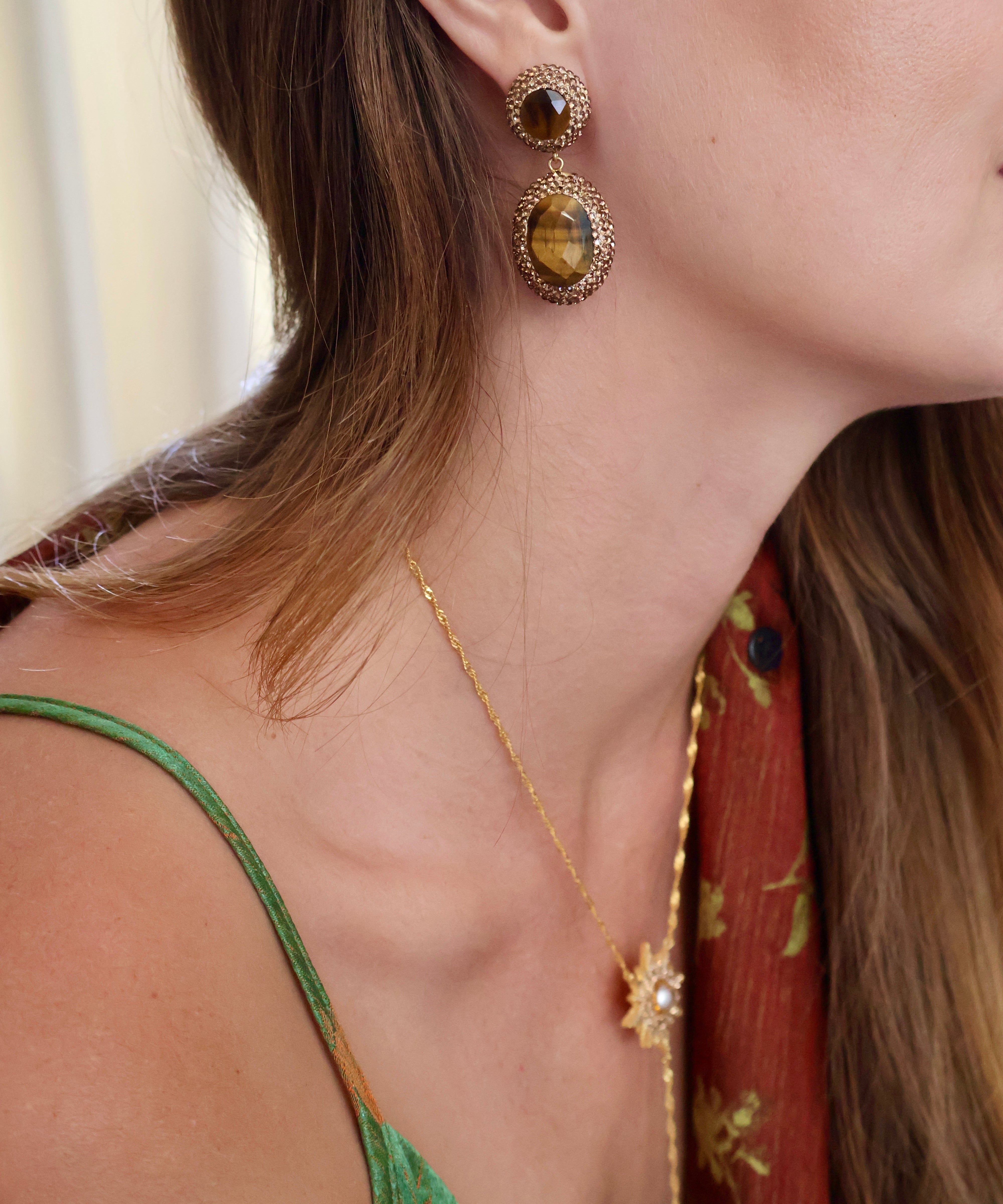 A close-up lifestyle shot of a model wearing a gold-toned double drop earring with tiger's eye stones and a matching gold necklace with a star and moon pendant.