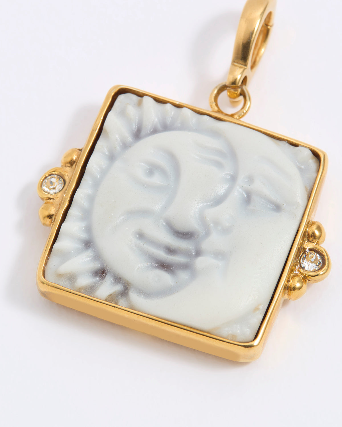 Gold-framed square pendant with a face of a sun and moon design set on a square tile on a white background
