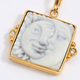 Gold-framed square pendant with a face of a sun and moon design set on a square tile on a white background