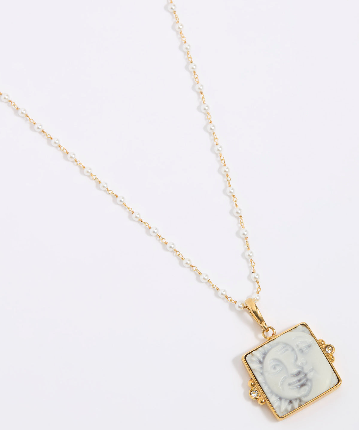 Gold-framed square pendant with a face of a sun and moon design set on a square tile hung from a peal chain on a white background