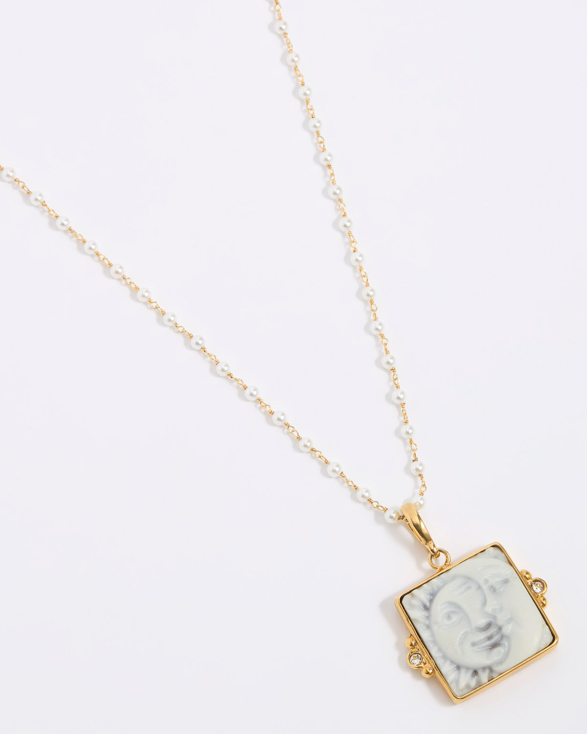 Gold-framed square pendant with a face of a sun and moon design set on a square tile hung from a peal chain on a white background
