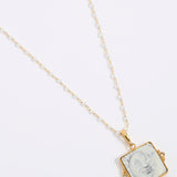 Gold-framed square pendant with a face of a sun and moon design set on a square tile hung from a peal chain on a white background