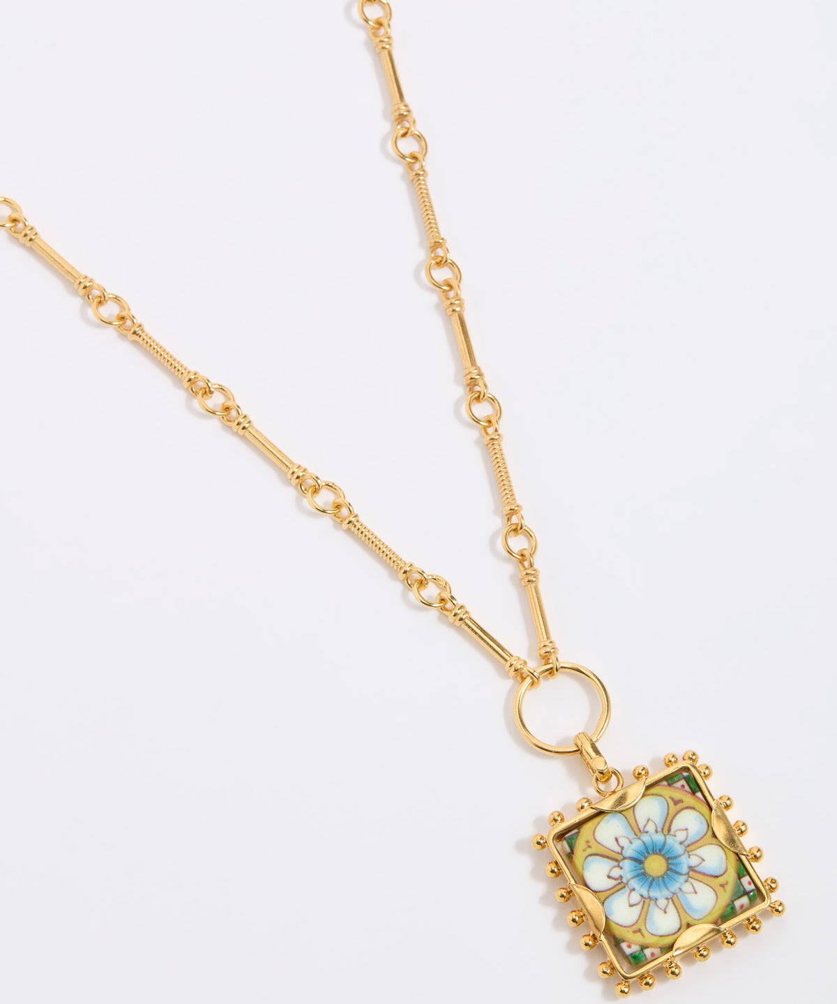 Gold square pendant with a floral tile design on a gold bar style chain on a white background 