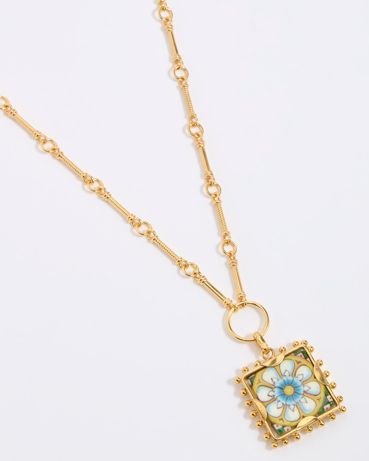 Gold square pendant with a floral tile design on a gold bar style chain on a white background 