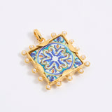 Decorative pendant with blue and gold design on a square tile with mini pearl edging  on a white background