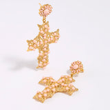Gold and pink cross-shaped earrings on a white background