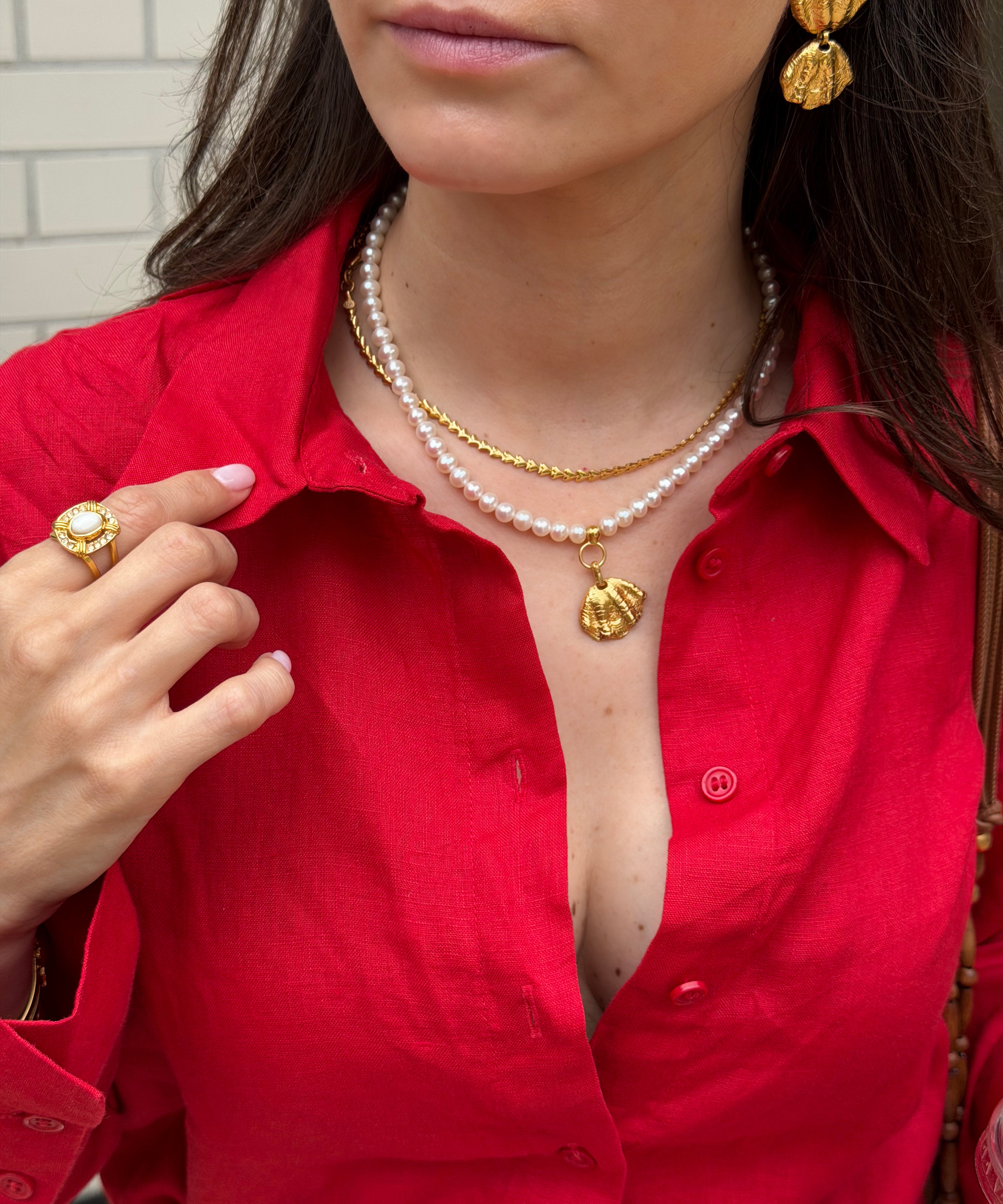 Woman wearing a red shirt with gold jewelry and a pearl necklace.