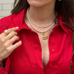 Woman wearing a red shirt with gold coloured jewelry and a pearl necklace.