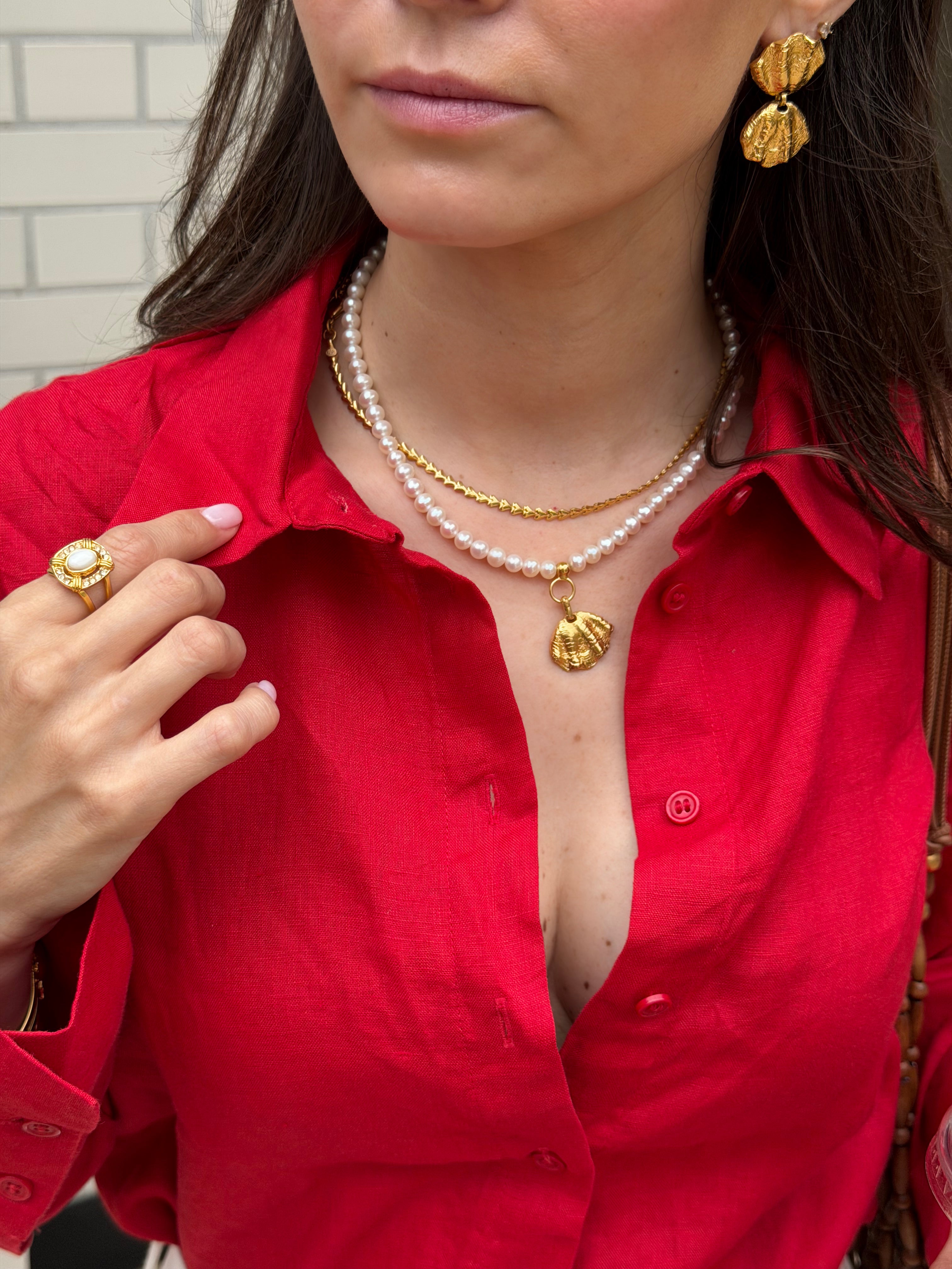 Woman wearing a red shirt with gold coloured jewelry and a pearl necklace.