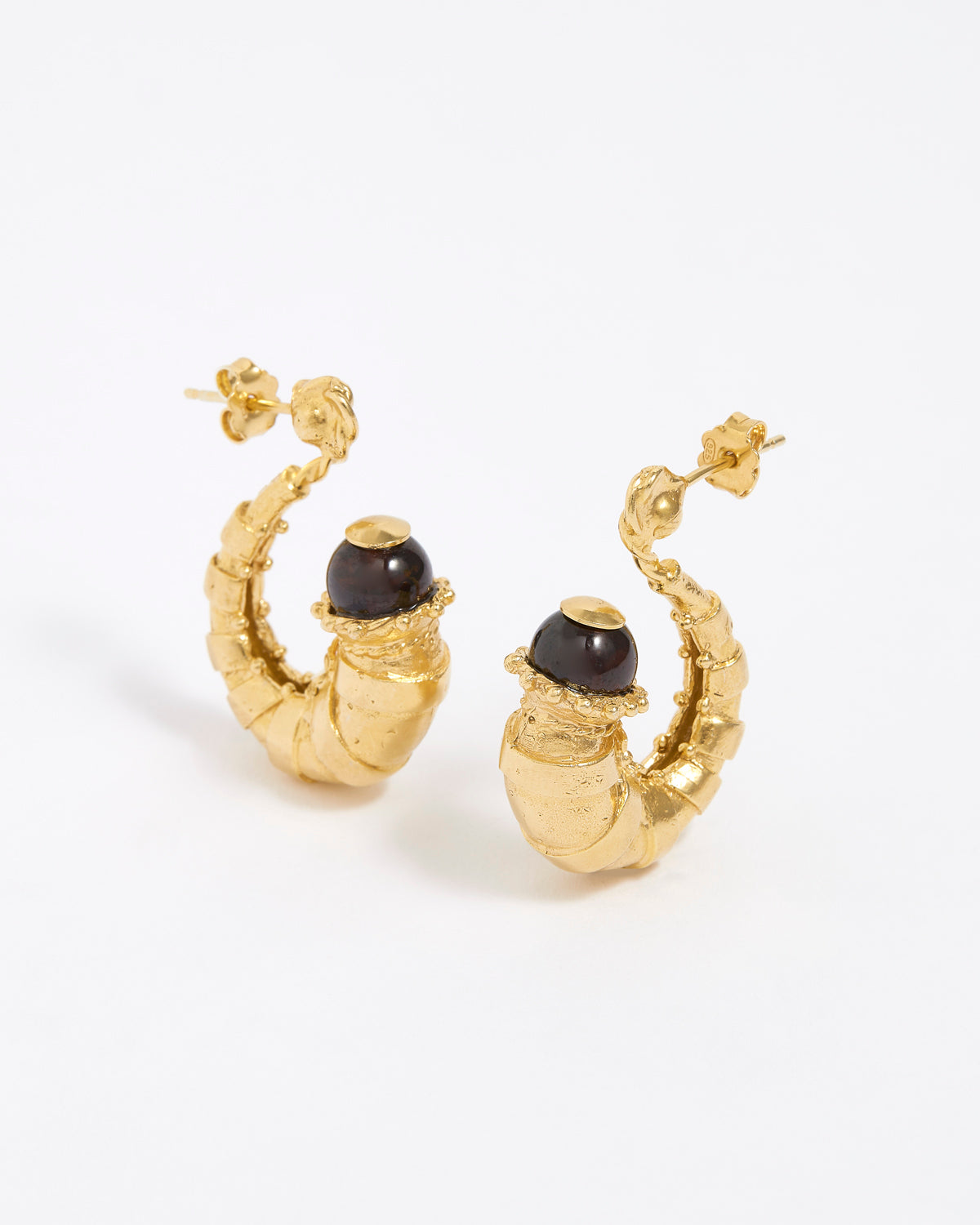 Gold half hoop earrings with dark brown gemstones on a white background