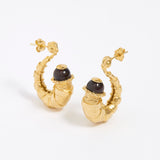 Gold half hoop earrings with dark brown gemstones on a white background