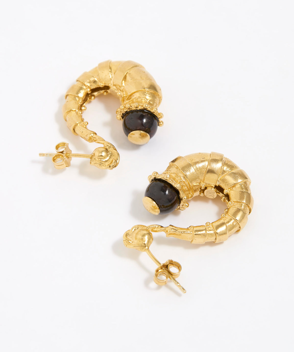Gold half hoop earrings with dark brown gemstones on a white background