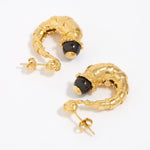 Gold half hoop earrings with dark brown gemstones on a white background