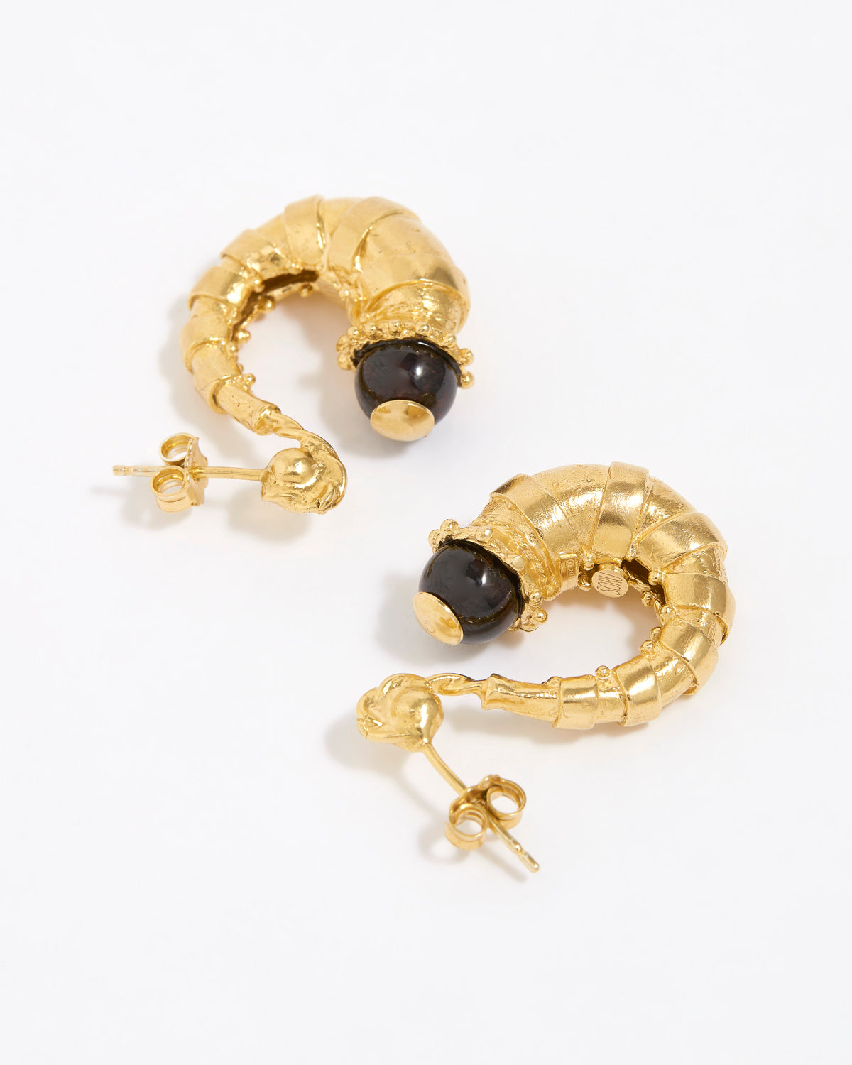 Gold half hoop earrings with dark brown gemstones on a white background